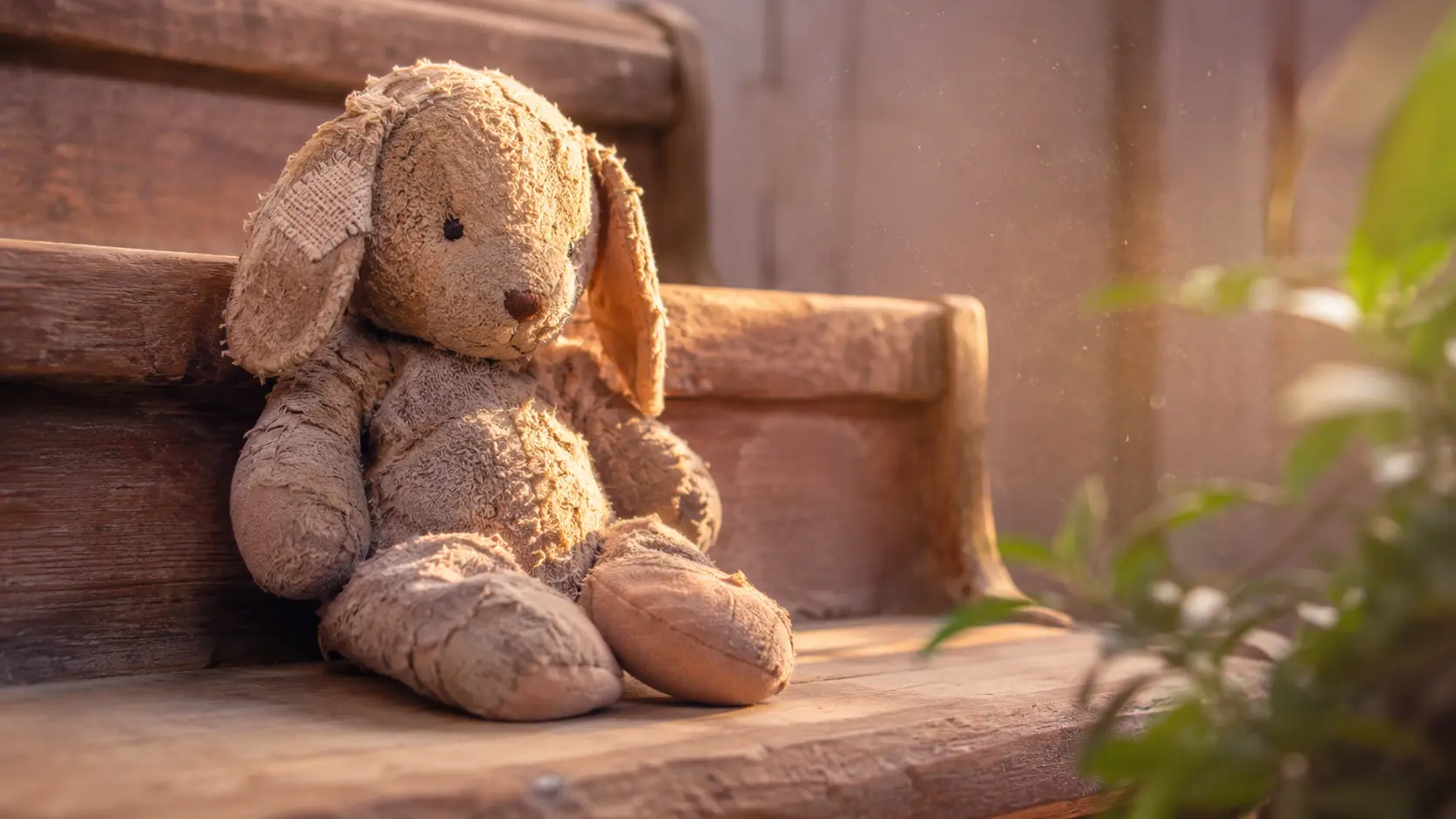 Ein altes, abgeliebtes Stofftier sitzt auf einer hölzernen Treppenstufe im warmen Nachmittagslicht, ein Ohr ist geflickt. Sinnbild für das Innere Kind.